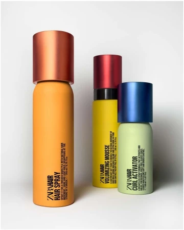 Three colorful ZARA hair product bottles in a studio setting: hair spray (orange), volumizing mousse (yellow), and curl activator (green).