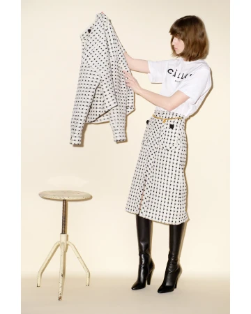 Model holding a patterned jacket wearing a matching skirt and black knee high boots by Raymond Meier