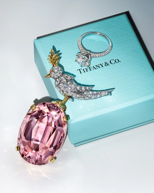Close-up of a bird-shaped brooch with a large pink gemstone, a diamond ring, and a Tiffany & Co. jewelry box, luxurious and elegant.