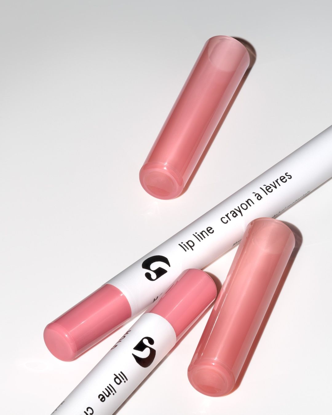 Close-up of two lip liner crayons with pink tips and two matching caps on a white surface, showcasing beauty product design.