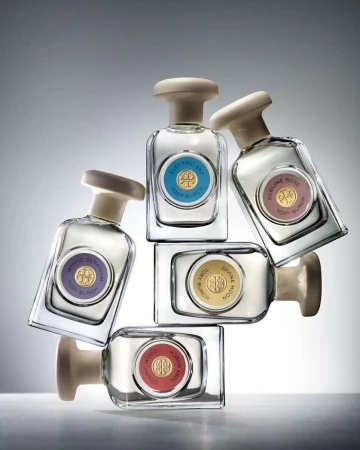 Stacked arrangement of Tory Burch perfume bottles in a gradient gray studio setting showcasing various fragrances and packaging designs.