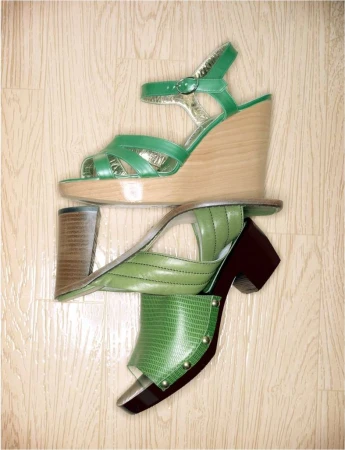 Overhead shot of three green women's shoes stacked on a light wood floor. A sandal, slide, and heel are arranged vertically.
