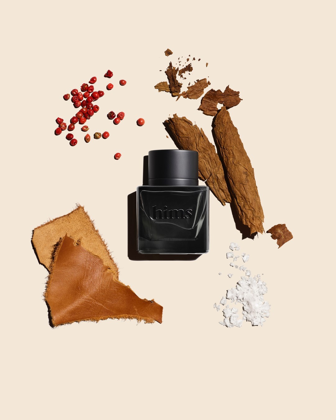 Close-up studio shot of black perfume bottle surrounded by aromatic elements like peppercorns, tobacco leaves, leather, and white powder.