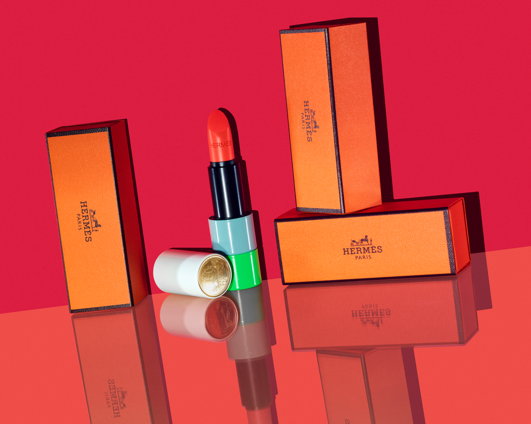 Hermes lipstick with opened and closed cases on a reflective red surface, studio lighting, beauty shot, modern cosmetics product.