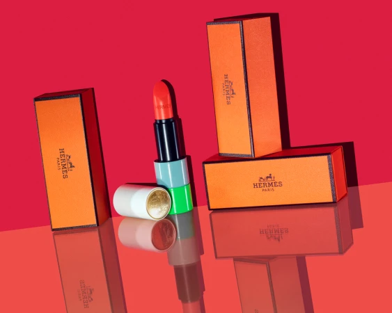 Hermes lipstick with opened and closed cases on a reflective red surface, studio lighting, beauty shot, modern cosmetics product.
