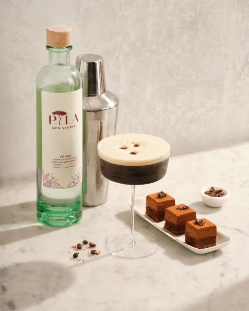 Espresso martini cocktail on marble surface with brownies, vodka bottle, and shaker. Drink photography for food and beverage industry.