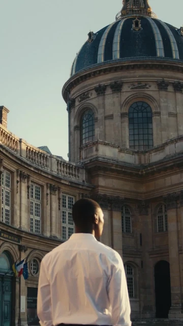 Man in white shirt looks toward architectural landmark featuring a dome; stone and windows, outdoors on a sunny day, vertical