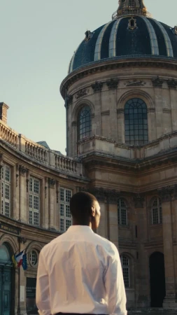 Man in white shirt looks toward architectural landmark featuring a dome; stone and windows, outdoors on a sunny day, vertical