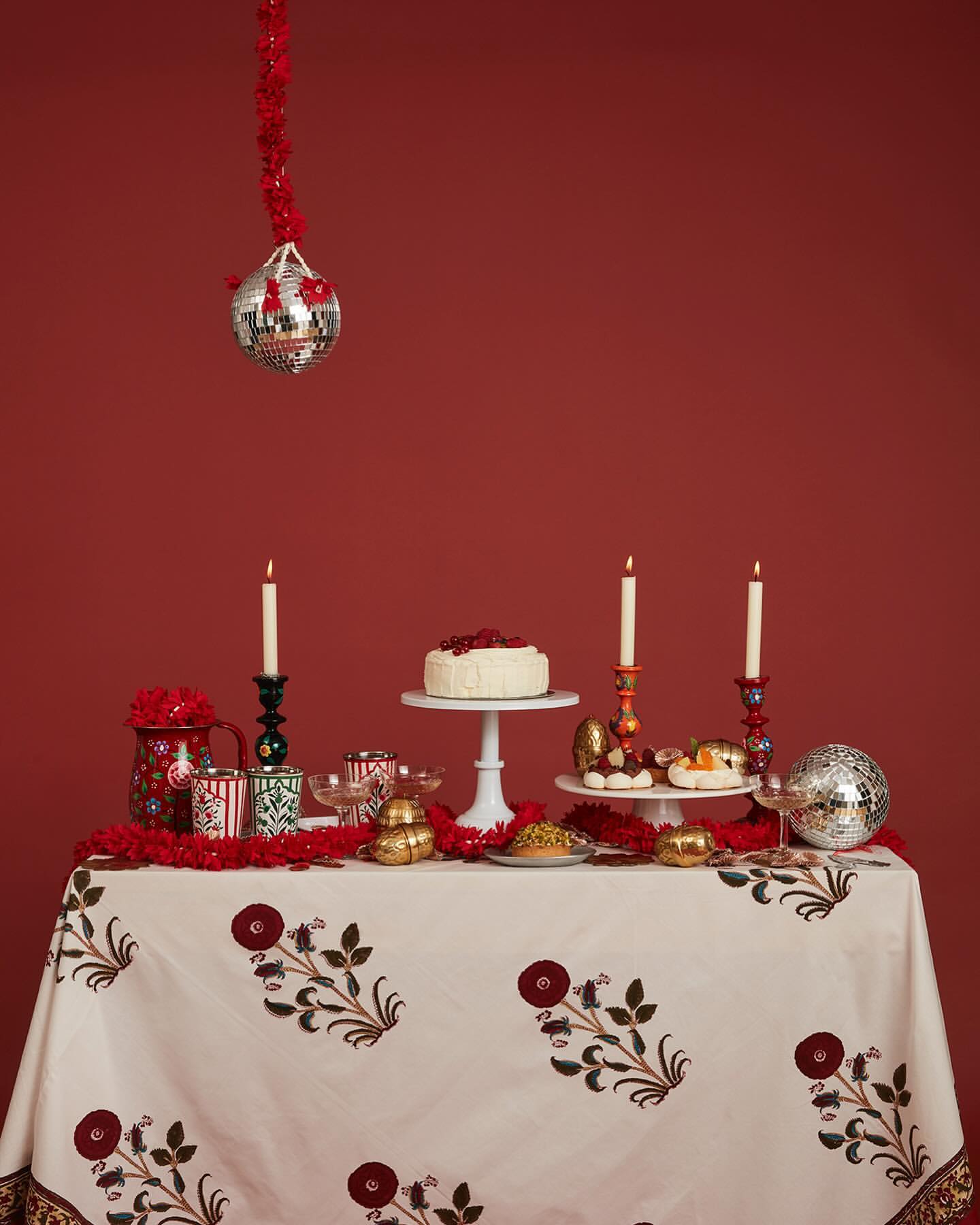 Festive dessert table featuring cake, pastries, candles, and disco balls against a red backdrop, creating a vibrant celebration scene.