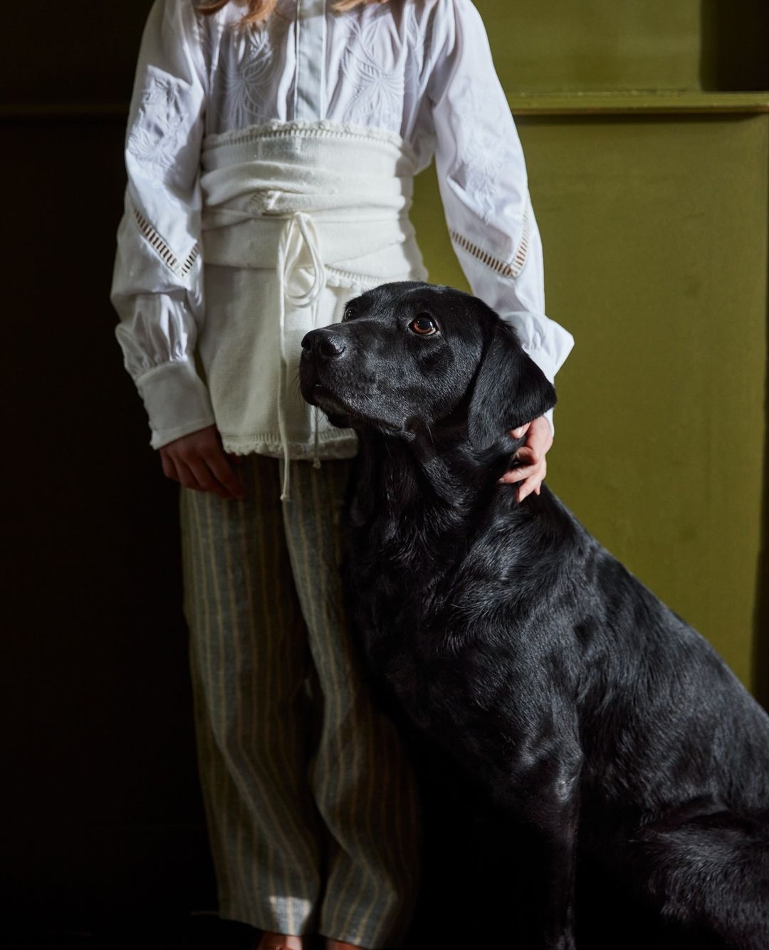Woman in white blouse with black dog in a studio setting. Portrait of female with black labrador retriever indoors in natural light.