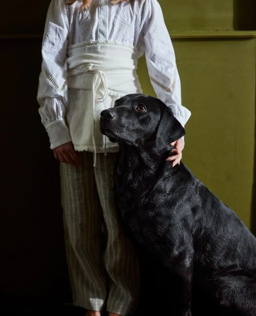 Woman in white blouse with black dog in a studio setting. Portrait of female with black labrador retriever indoors in natural light.