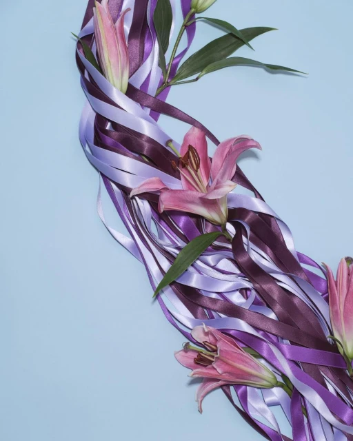 Floral display of pink lilies and purple ribbon against a light blue background, creating a soft, elegant, and visually appealing composition.