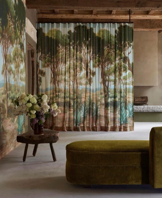 Olive green sofa and rustic wood table with white flowers in an interior space featuring curtain with landscape painting design.