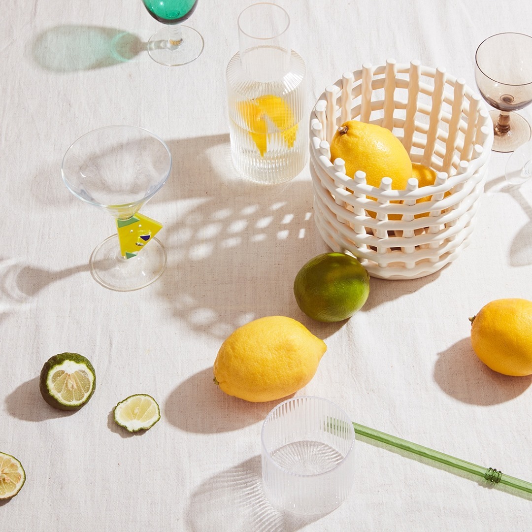 Overhead shot of lemons, limes, and glassware on a white tablecloth, capturing a refreshing and vibrant still life composition.