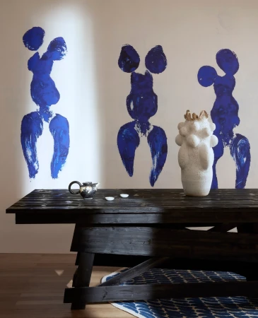 Minimalist interior with black wooden table, teapot, abstract art, and modern vase against a white wall with soft, natural lighting.