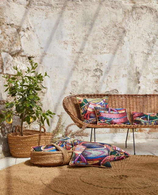 Outdoor living space with a woven bench and patterned pillows, a potted lemon tree, and a round woven rug on a stone patio.