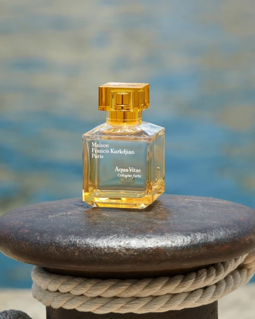 Elegant fragrance bottle by Maison Francis Kurkdjian Paris, Aqua Vitae, on a textured grey surface with a blurred blue and white background.