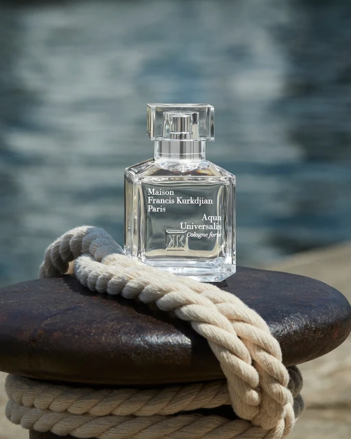 Crystal bottle of Maison Francis Kurkdjian Aqua Universalis cologne on a dark metal surface with a thick nautical rope. 