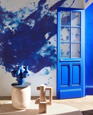Interior shot of a room featuring a blue door and a blue vase on a table, complemented by a unique sculptural design and abstract wall art.
