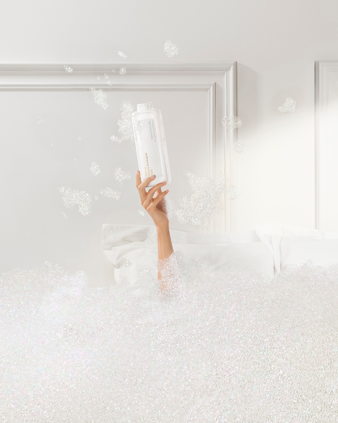 Arm holding white bottle in a white bubble bath against a white background with a white door frame for bath and beauty advertising.