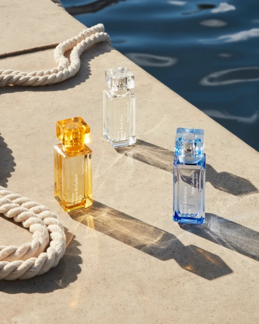 Three perfume bottles arranged on a stone surface near water with a nautical rope, showcasing beauty product photography in natural light.