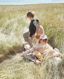 Three children playing outdoors in tall dry grass, photographed by Rebecka Oftedal.