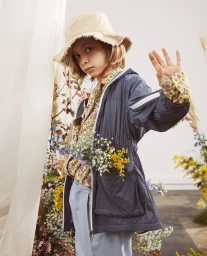 Child wearing a bucket hat, patterned shirt, and blue windbreaker holding flowers, photographed by Rebecka Oftedal