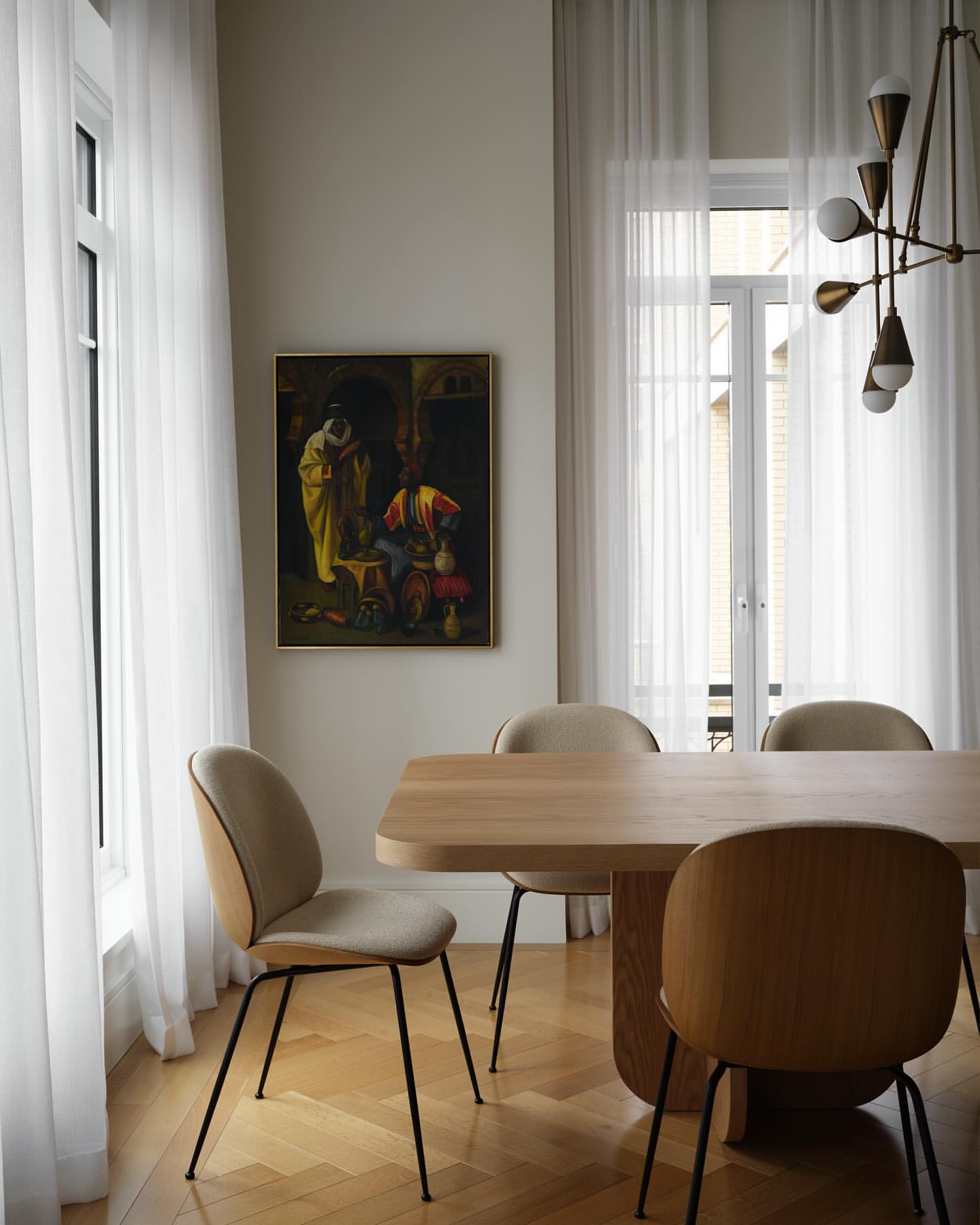Interior dining room with a light wood table surrounded by chairs, featuring a framed painting on the wall near a window with white curtains.