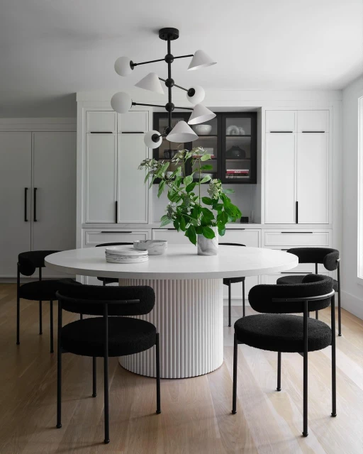 Modern dining room features a white round table, black upholstered chairs, a statement chandelier, and built-in cabinetry, creating a stylish space.