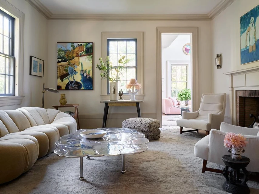 Living room interior with a curved sofa, flower-shaped coffee table, and armchairs, illuminated by natural light from the windows, creating a serene atmosphere.