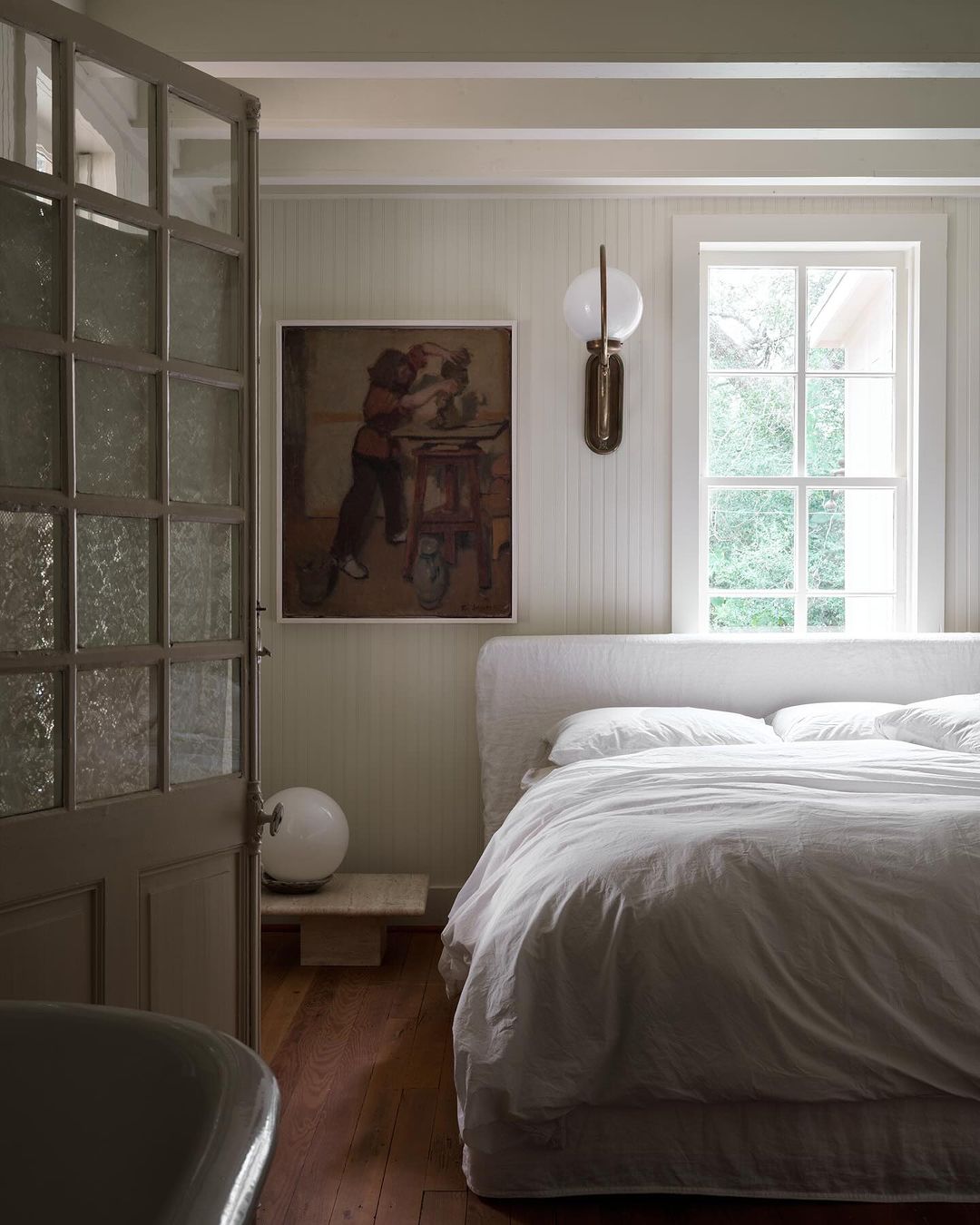 Bedroom interior with a made-up bed, a painting on the wall, and an open door, capturing a cozy and inviting space.