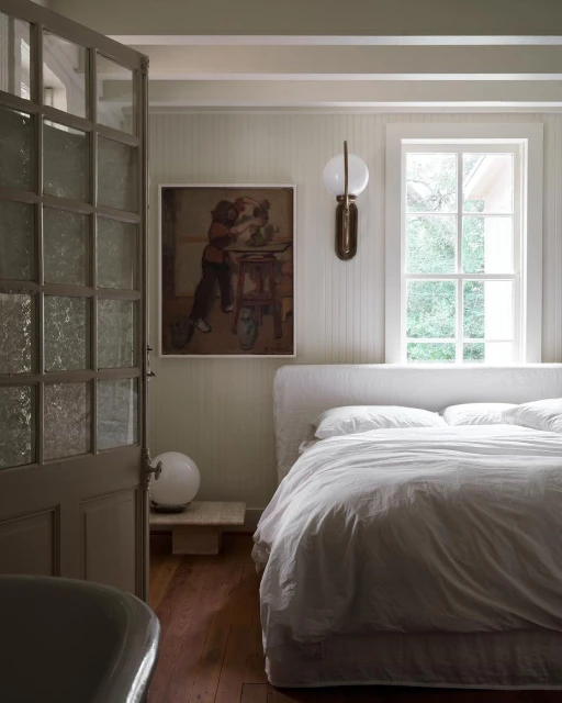 Bedroom interior with a made-up bed, a painting on the wall, and an open door, capturing a cozy and inviting space.