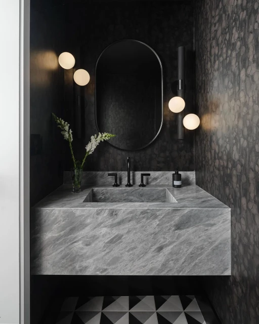 Bathroom interior featuring a marble countertop with sink, oval mirror, globe sconces, and geometric tile flooring in a modern style.