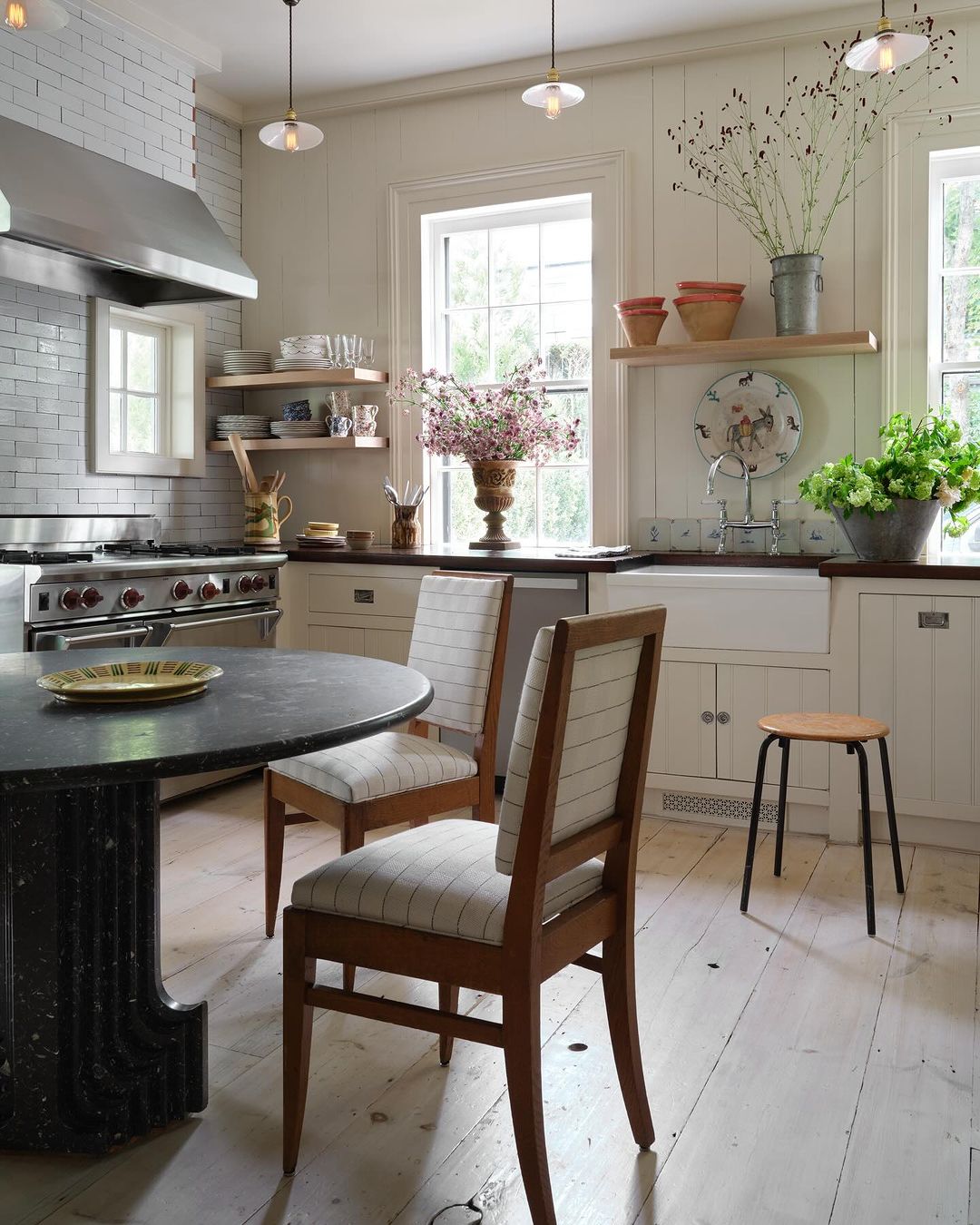 Bright kitchen interior with a wooden dining table, chairs, and vintage decor. The modern stove and sink area create a functional space.