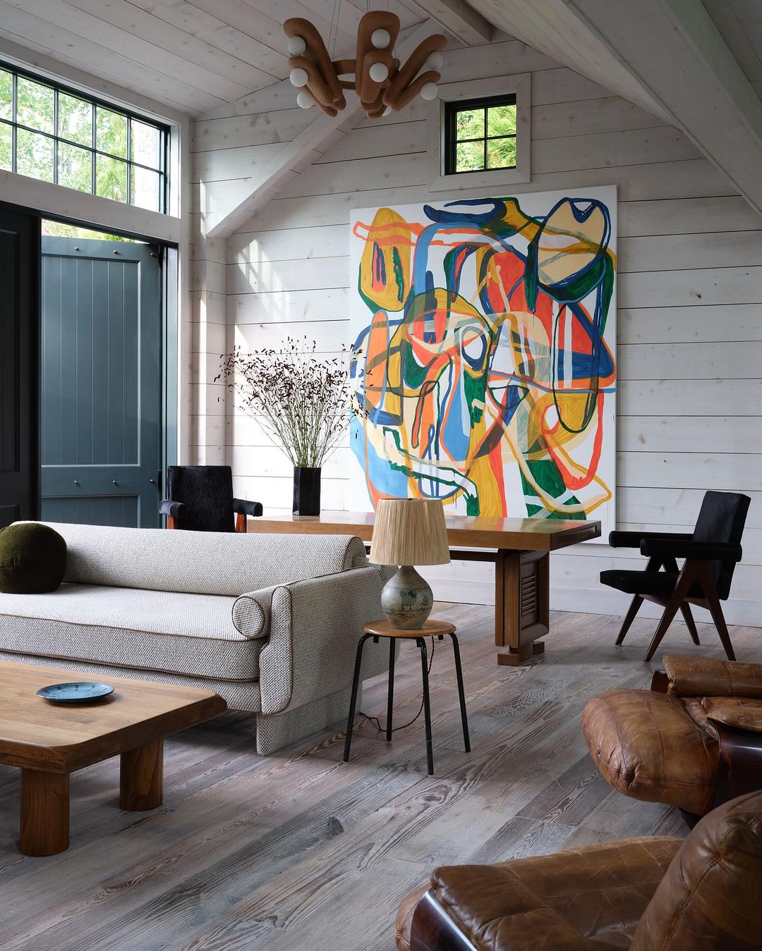 Living room interior featuring a light grey sofa, wooden coffee table, a large abstract painting, and a unique wooden chandelier.