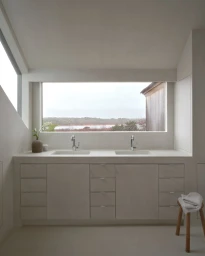 Minimalist bathroom interior featuring a double vanity sink below a wide horizontal window framing an outdoor landscape.