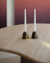 Two white taper candles in brass holders sitting on a curved beige stone table against a gradient background.