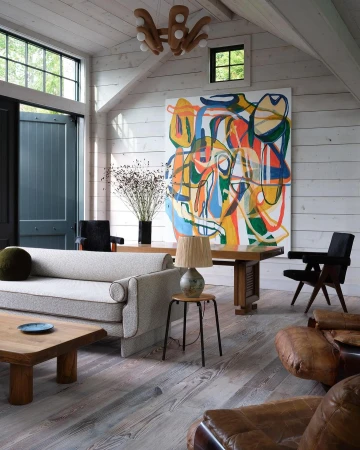 Spacious modern living room with white wood-paneled walls, a light grey sofa, wooden coffee table, and large abstract painting.