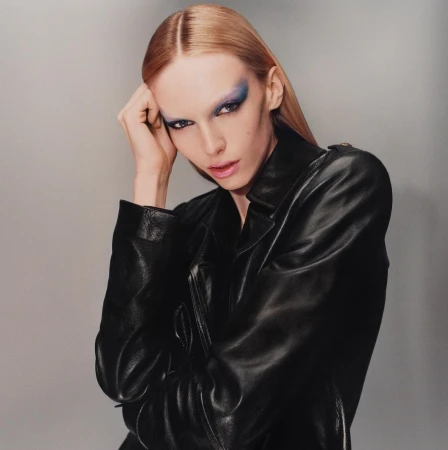 Model with blue eyeshadow wearing a black leather jacket against a neutral grey background