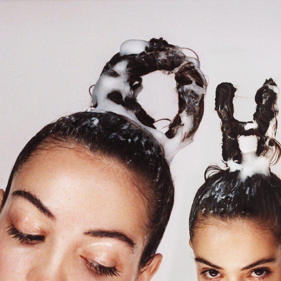 Two women with dark hair styled with foamy shampoo. The hairstyle is formed into abstract shapes against a white background.