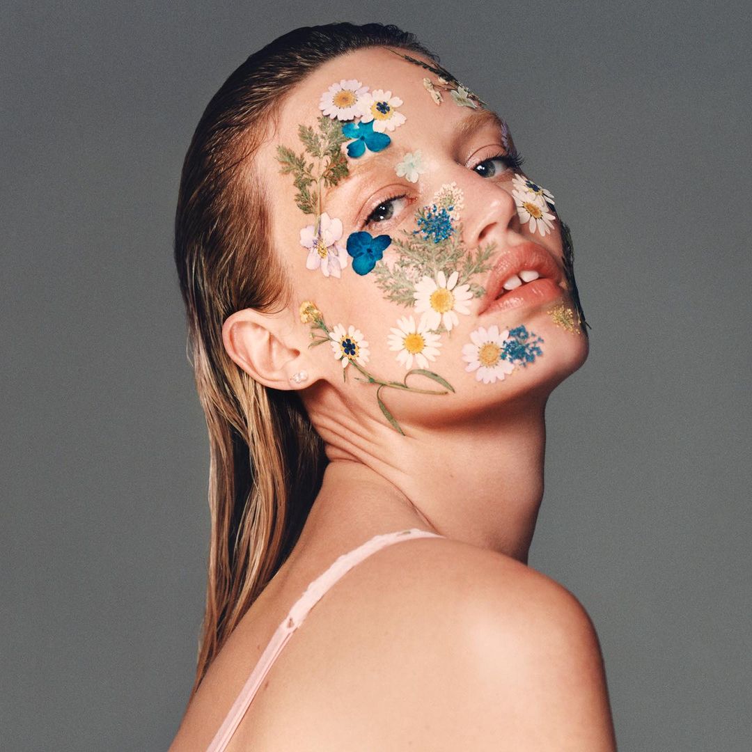 Close-up portrait of a woman with wet hair and pressed dried wildflowers adhered to her face, photographed by Rémi Lamandé