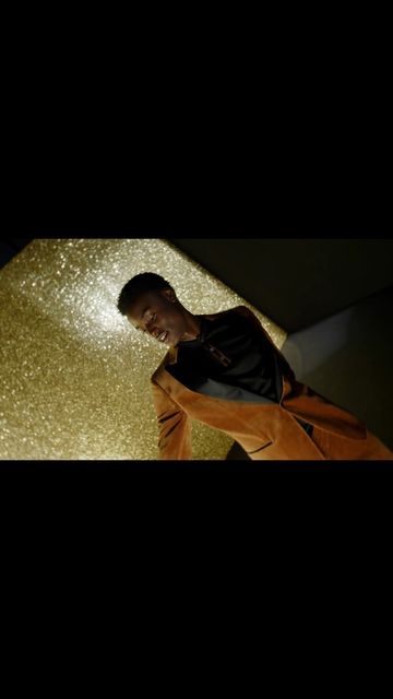 Person in orange and black jacket with gold glittery background looking down in a dimly lit room, close-up shot.