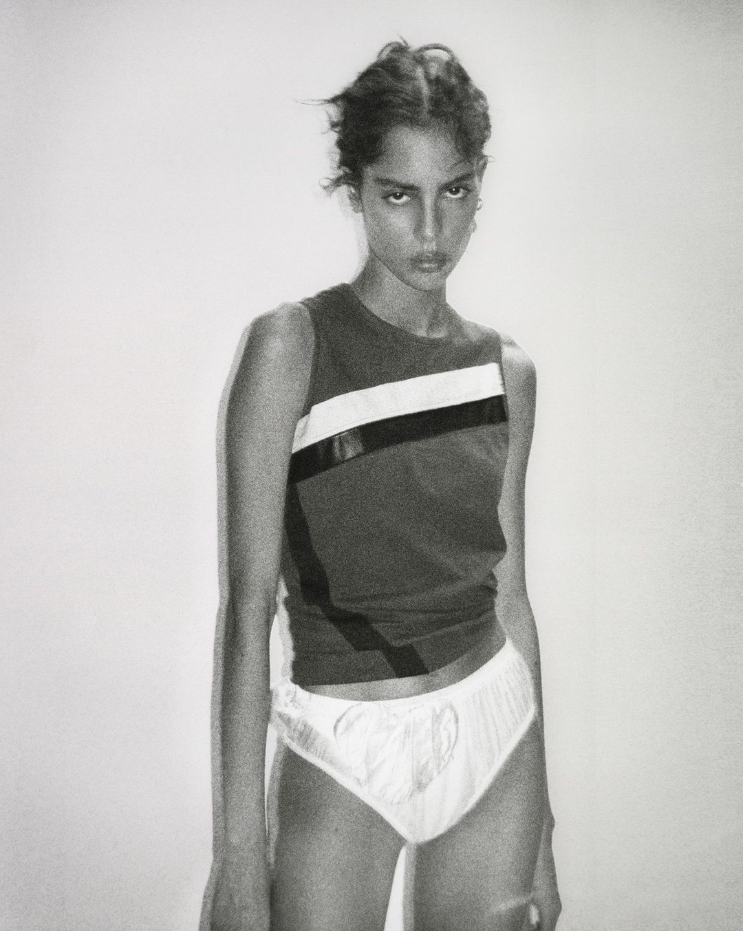Portrait of a female model wearing a sleeveless colorblocked top against a plain white wall by Remi Lamande.
