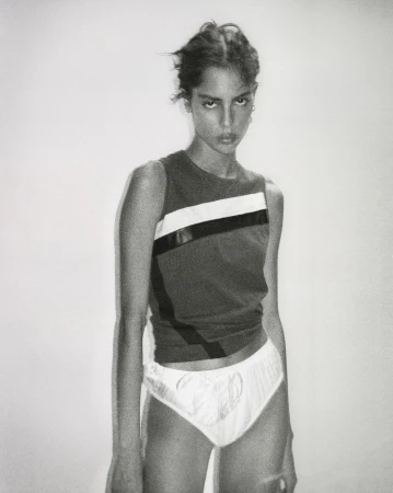 Portrait of a female model wearing a sleeveless colorblocked top against a plain white wall by Remi Lamande.