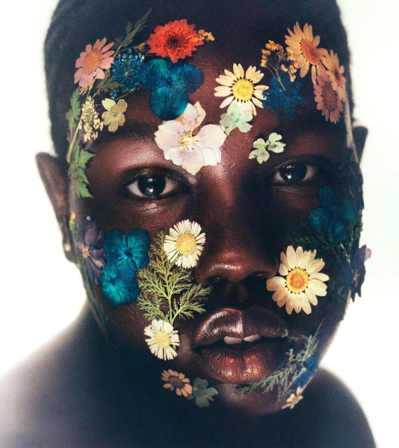 Portrait of a Black woman with flowers on her face. The flowers include daisies, pansies and others in orange, blue and white hues.