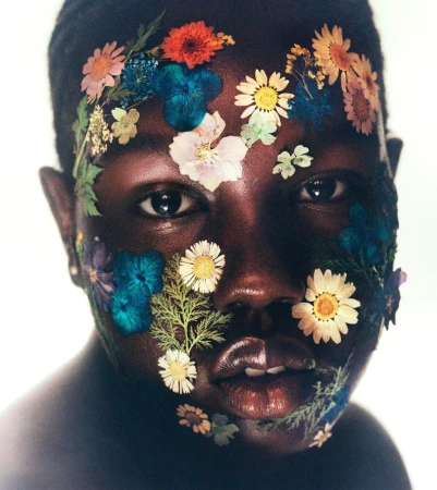 Portrait of a Black woman with flowers on her face. The flowers include daisies, pansies and others in orange, blue and white hues.
