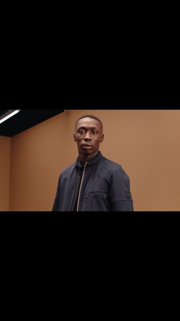 Portrait of an adult male wearing a dark jacket in an indoor setting with tan colored walls, gazing off to the side.