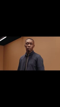 Portrait of an adult male wearing a dark jacket in an indoor setting with tan colored walls, gazing off to the side.