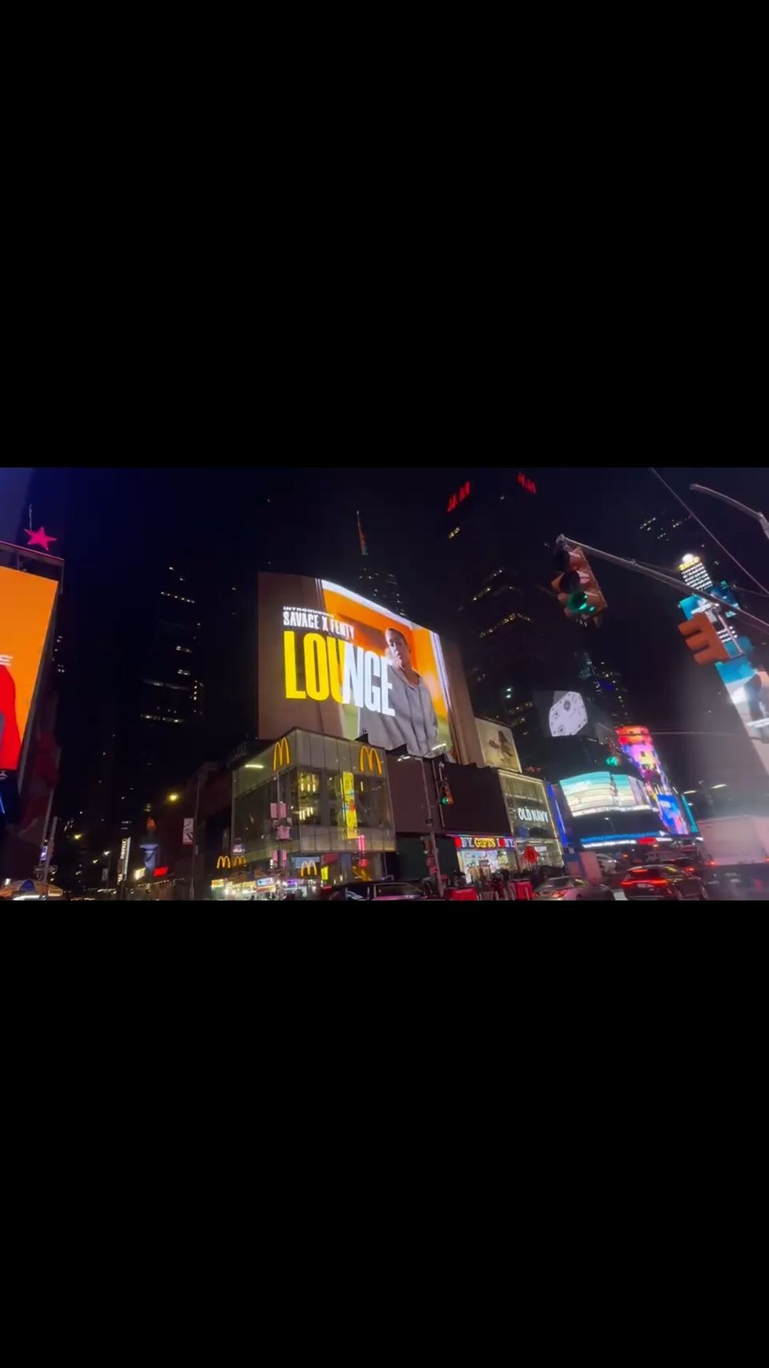 Illuminated billboard in Times Square at night showcasing a person, set against a backdrop of buildings and signage.