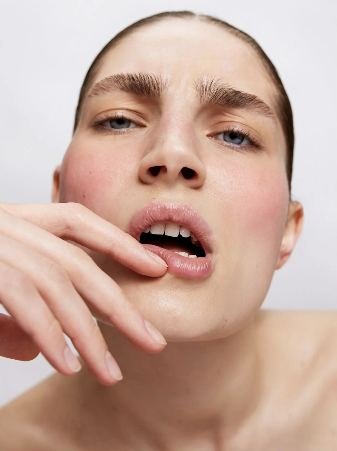 Close-up beauty shot of a young adult woman with fair skin, blue eyes, and light pink lipstick, posing against a white background.